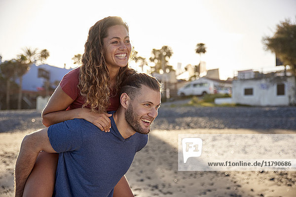 Young man giving his girlfriend a piggyback ride on the beach