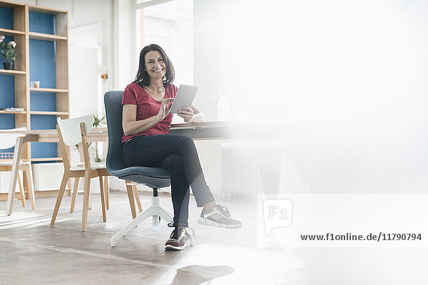 Portrait of smiling woman with tablet sitting at desk in a loft