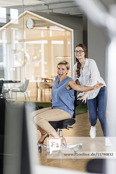 Playful employee pushing colleague on office chair