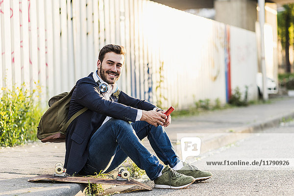 Smiling young man sitting on pavement holding cell phone
