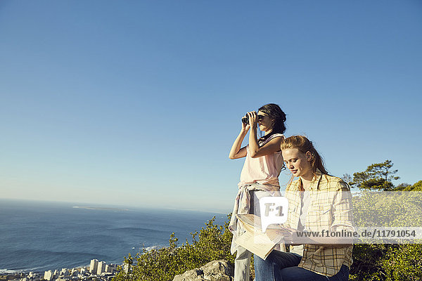 Südafrika  Kapstadt  Signal Hill  zwei junge Frauen mit Karte und Fernglas mit Blick aufs Meer