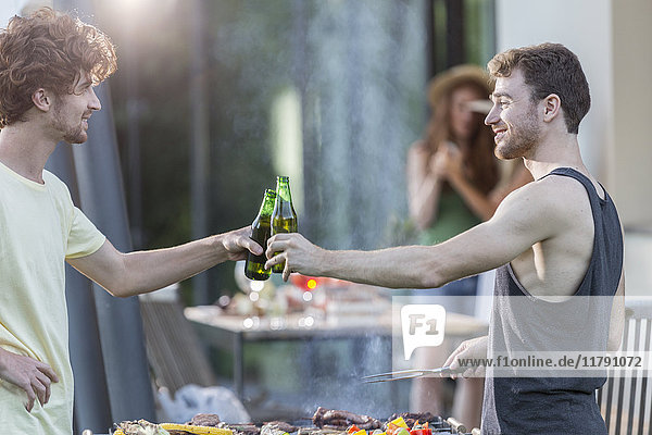 Two men clinking beer bottles at barbecue grill