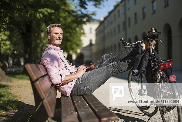 Mann mit Fahrrad und altmodischer Kamera entspannt auf einer Parkbank