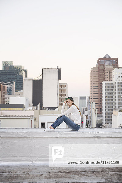 Junge Frau auf Balustrade einer Dachterrasse sitzend