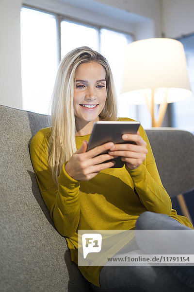 Portrait of smiling woman sitting on couch using mini tablet