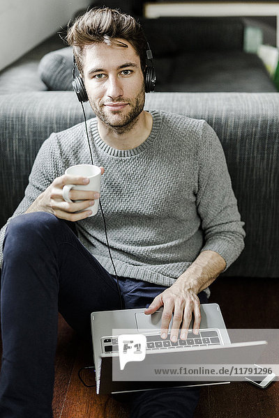 Porträt eines selbstbewussten jungen Mannes mit Laptop und Kopfhörer zu Hause