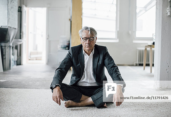 Senior Geschäftsmann auf dem Boden sitzend meditierend