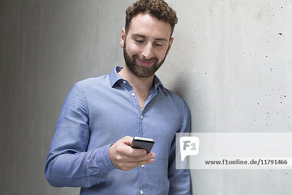Smiling man looking at cell phone at concrete wall