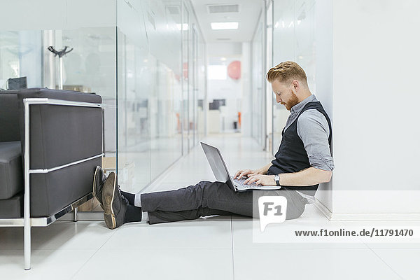 Geschäftsmann im Büro sitzend auf dem Boden  mit Laptop