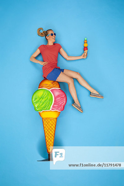 Woman sitting on big icecream cone  eating a small one