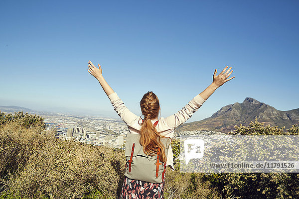 Südafrika  Kapstadt  Signal Hill  glückliche junge Frau mit erhobenen Armen mit Blick auf die Stadt