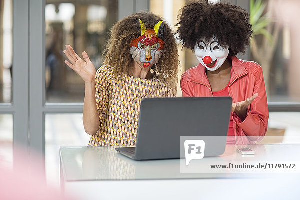 Zwei Frauen im Büro tragen Masken und teilen sich einen Laptop.