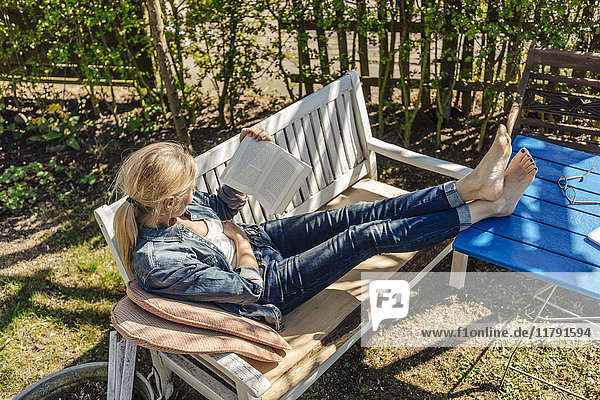 Frau liest Buch auf Gartenbank
