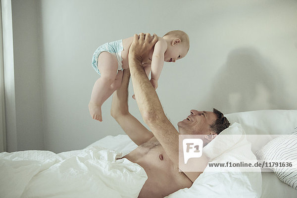 Glücklicher reifer Vater hebt seinen kleinen Sohn im Bett auf