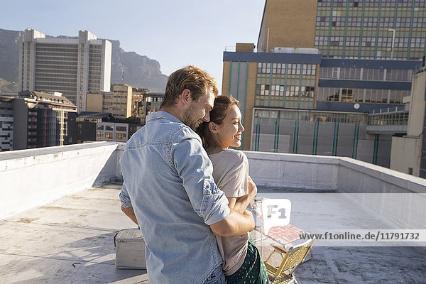 Young couple celebrating on a rooftop terrace  embracing at sunset