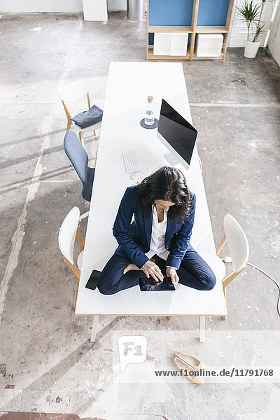 Geschäftsfrau sitzt auf dem Schreibtisch in einem Loft mit Tablette