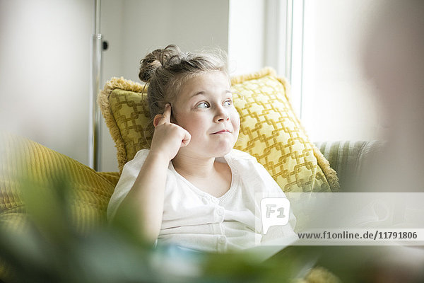 Porträt eines denkenden kleinen Mädchens sitzend mit Zeitschrift auf Sessel