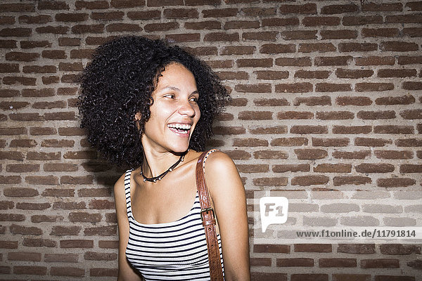 Portrait of laughing woman in front of brick wall at night