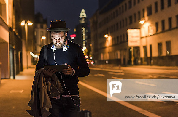 Stilvoller junger Mann mit Tablette auf der Stadtstraße bei Nacht