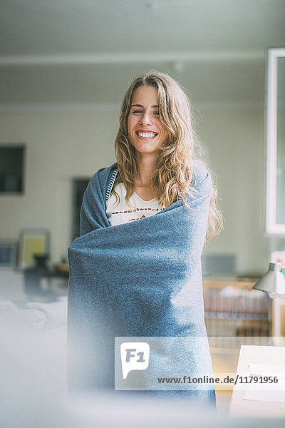 Fröhliche junge Frau zu Hause in eine Decke gehüllt