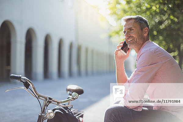 Lächelnder Mann mit Fahrrad am Telefon auf einer Parkbank