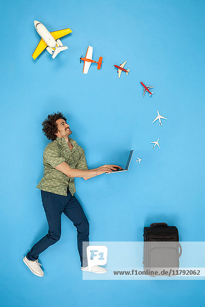 Mann mit Koffer schaut auf Flugzeuge  die aus seinem Laptop kommen.