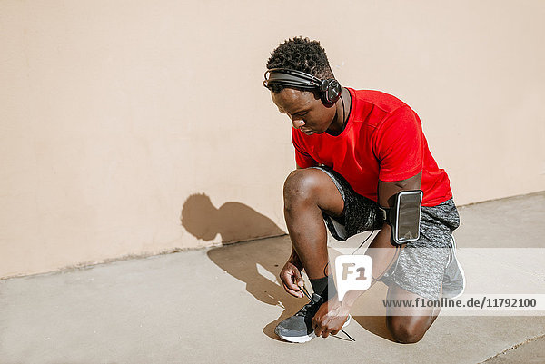 Mann in Sportbekleidung  der seine Schuhe bindet  während er Musik über Kopfhörer hört.