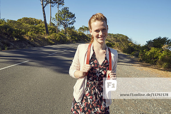 Südafrika  Kapstadt  Signal Hill  lächelnde junge Frau mit Rucksack auf der Landstraße