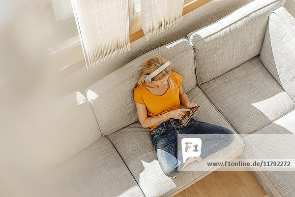 Frau zu Hause sitzend auf der Couch mit Kopfhörer und Tablett