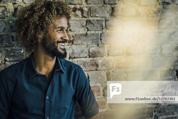 Smiling man with beard and curly hair at brick wall