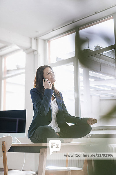 Businesswoman on the phone doing yoga exercise on desk in a loft