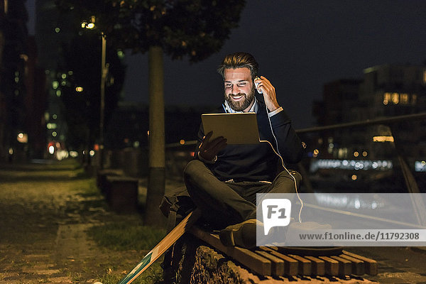 Smiling young man with tablet and headphone in the city at night