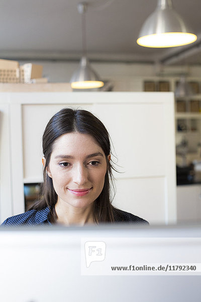 Lächelnde Frau schaut auf den Computerbildschirm am Schreibtisch im Büro