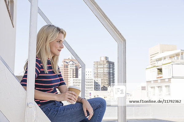 Young woman drinking coffee  sitting on stairs on a rooftop terrace