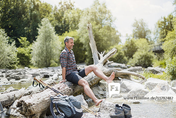 Wanderer macht eine Pause am Flussufer und spritzt mit den Füßen ins Wasser.