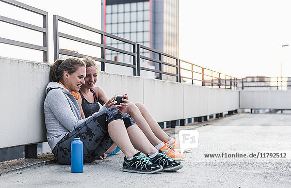 Two women having a break from exercising sharing smartphone