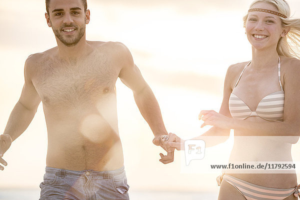 Ein junges Paar  das am Strand rennt und Händchen hält.