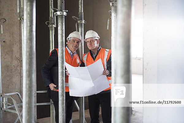 Two men with plan wearing safety vests in building under construction
