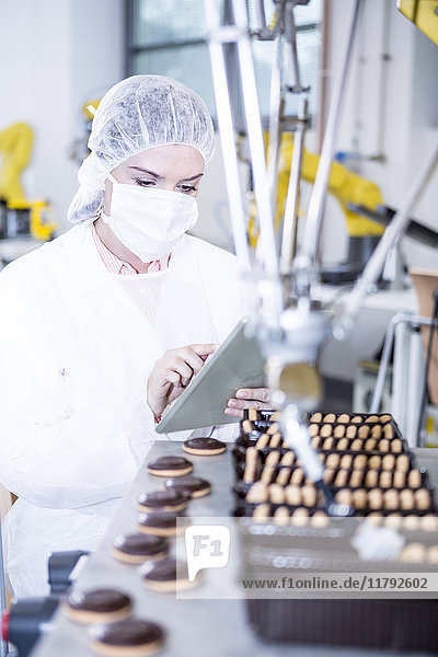 Frau in der Fabrik mit Tablette und Roboter beim Umgang mit Cookies