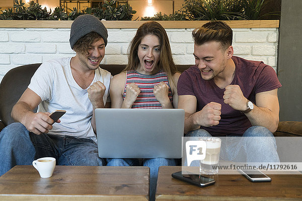 Three excited friends looking at laptop in a cafe