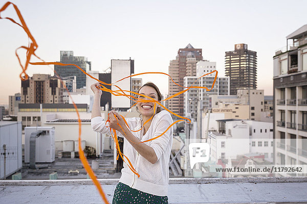 Young woman standing on a rooftop terrace  playing with a ribbon