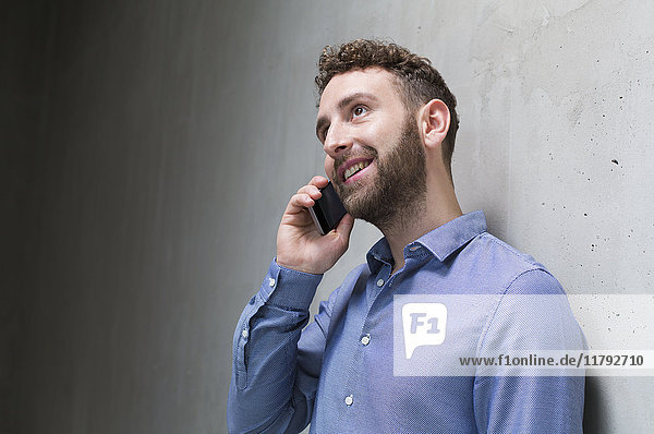 Smiling man on cell phone at concrete wall