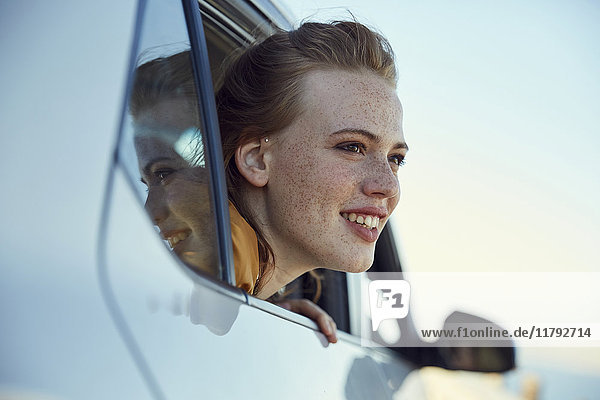 Lächelnde junge Frau  die aus einem Auto schaut.