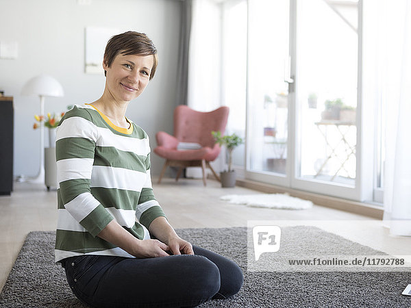 Porträt einer lächelnden Frau  die im Wohnzimmer auf dem Boden sitzt.