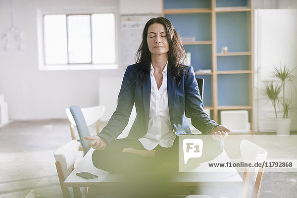 Businesswoman doing yoga exercise on desk in a loft