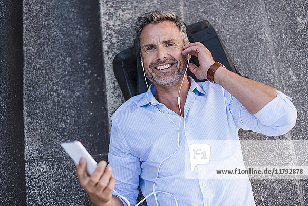 Lächelnder Mann auf der Treppe liegend mit Handy und Ohrstöpseln