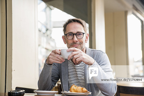 Portrait of smiling mature man drinking coffee in a sidewalk cafe