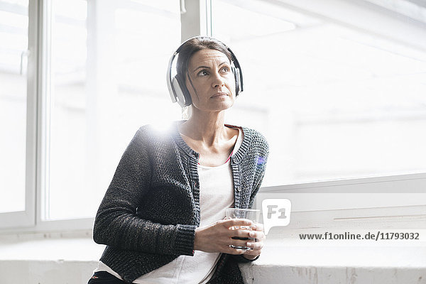 Porträt einer Frau in einem Loft  die Musik mit Kopfhörern hört