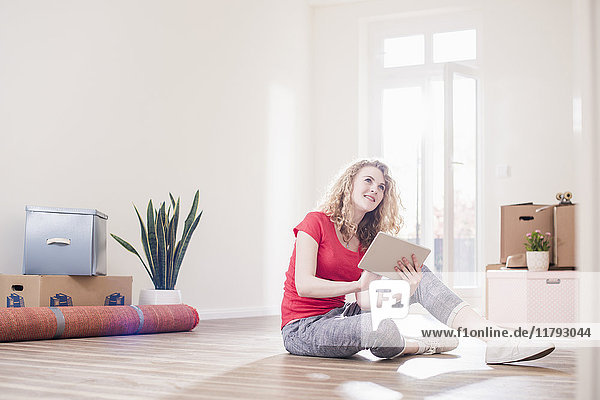 Junge Frau im neuen Zuhause sitzend auf dem Boden mit Tablette