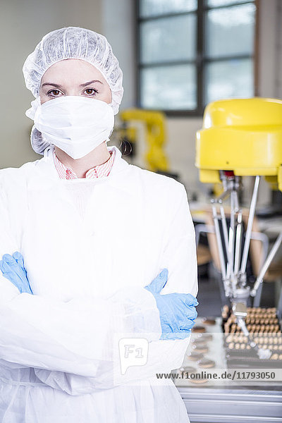 Porträt einer Frau in Arbeitsschutzbekleidung mit Roboter  der Kekse im Hintergrund handhabt